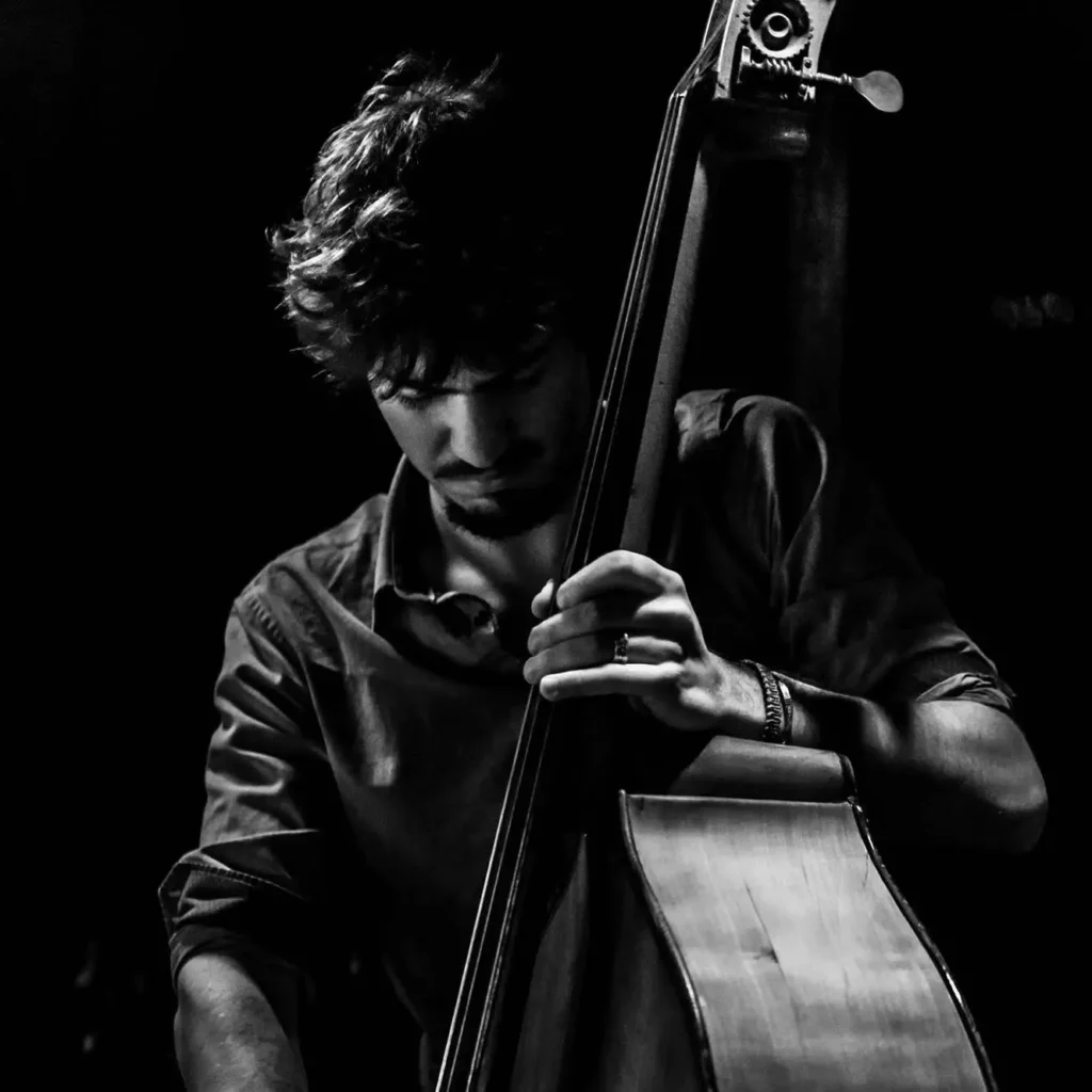 Photographie en noir et blanc de Benjamin Lopez jouant de la contrebasse, le regard baissé vers son instrument, sur une scène sombr